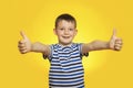 Portrait of happy boy in striped t-shirt showing thumbs up gesture on yellow background Royalty Free Stock Photo