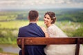 Portrait of a happy bride sitting on a bench on the top of the hill with the groom and looking back Royalty Free Stock Photo