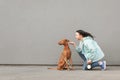 Portrait of a happy brunette woman in casual clothes in the street with a dog on a leash, owner plays with a pet at the background