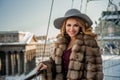 Portrait of happy brunette woman wearing re ress, fur mink winter coat and grey hat on the background of city Royalty Free Stock Photo