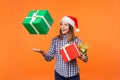 Portrait of happy brunette young woman in santa hat and checkered shirt standing throwing gift boxes in air or catching presents, Royalty Free Stock Photo