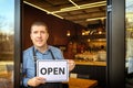 Portrait of happy business owner holding open sign - Young man entrepreneur at entrance of new small family restaurant inviting pe Royalty Free Stock Photo