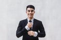 Portrait of Happy Businessman in Black Formal Suit. Standing by the Cement Wall, Touching Neck Ties