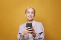 Portrait of a happy businesswoman using mobile phone and smiling against colorful yellow studio wall background Royalty Free Stock Photo