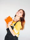 Portrait of happy carefree smiling teenager girl with dark long hair in yellow t-shirt with copybook on grey background Royalty Free Stock Photo