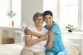 Portrait of happy caregiver together with senior patient sitting on bed in retirement home Royalty Free Stock Photo