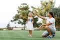 Portrait of a happy caring father teaching his small pretty daughter how launching a toy plane in a green park smiling full