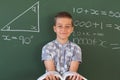 Portrait of happy caucasian boy standing at chalkboard in maths lesson classroom holding schoolbook