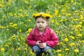 Portrait of happy caucasian child of four years old with wreath on head sitting on meadow of dandelions looking at camera