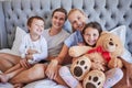 Portrait of a happy caucasian family with two children sitting on a bed holding teddybear and smiling at the camera Royalty Free Stock Photo