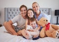 Portrait of a happy caucasian family with two children sitting on a bed holding teddybear and smiling at the camera Royalty Free Stock Photo