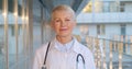 Portrait of happy caucasian female doctor standing outside hospital building and smiling at camera Royalty Free Stock Photo