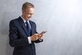 Portrait of Happy Caucasian Man in Blue Suit Holding Red Cellphone in Hands. Against Gray Grunge Wall