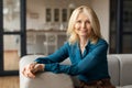 Portrait of happy caucasian mature woman smiling, looking at camera, sitting on comfy couch in living room interior Royalty Free Stock Photo