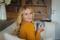 Portrait of happy caucasian woman sitting on couch in living room holding coffee cup and smiling Royalty Free Stock Photo