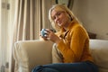 Portrait of happy caucasian woman sitting on couch in living room holding coffee cup, smiling Royalty Free Stock Photo