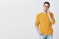 Portrait of happy charismatic young handsome man in glasses and yellow trendy sweater holding hand in pocket relaxed and