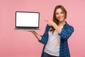 Portrait of happy charming girl in checkered shirt showing blank laptop screen and smiling, pointing mock up Royalty Free Stock Photo