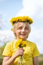 Portrait of happy cheerful blond boy with wreath of dandelions and bouquet of flower. Vertical frame. Sunny day Royalty Free Stock Photo