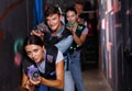 Portrait of happy young friends playing laser tag game with laser guns in dark corridor