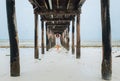 Portrait of a happy cheerful smiling woman dressed in light summer clothes walking barefoot under the sandy beach wooden pier. Royalty Free Stock Photo