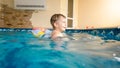 Portrait of happy cheerful toddler boy playing with inflatable beach ball and colorful ring at indoor swimming pool in Royalty Free Stock Photo