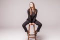 Portrait of a happy cheerful woman in black sitting on the chair and looking at camera over gray background Royalty Free Stock Photo