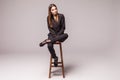 Portrait of a happy cheerful woman in black sitting on the chair and looking at camera over gray background Royalty Free Stock Photo