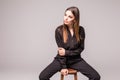 Portrait of a happy cheerful woman in black sitting on the chair and looking at camera over gray background Royalty Free Stock Photo