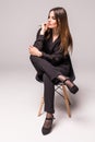 Portrait of a happy cheerful woman in black sitting on the chair and looking at camera over gray background Royalty Free Stock Photo