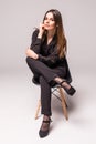 Portrait of a happy cheerful woman in black sitting on the chair and looking at camera over gray background Royalty Free Stock Photo