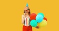 Portrait of happy cheerful young woman in festive birthday hat celebrating with bunch of colorful balloons having fun wearing