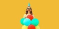 Portrait of happy cheerful young woman in festive birthday hat celebrating with bunch of colorful balloons having fun wearing