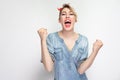 Portrait of happy cheering beautiful young woman in casual blue denim shirt with makeup and red headband standing, screaming and