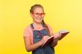 Portrait of happy clever little girl in red glasses holding notebook and pencils, smiling at camera, writing creative idea Royalty Free Stock Photo
