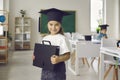 Portrait of happy pretty little student girl in academic cap standing in classroom Royalty Free Stock Photo