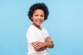 Portrait of happy and confident little boy in white T-shirt standing with crossed hands and smiling at camera Royalty Free Stock Photo