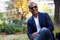 Portrait of Happy confident young African-American businessman in formal wear and sunglasses sitting at city park Royalty Free Stock Photo