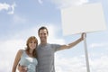 Portrait of happy couple with blank sign board against cloudy sky Royalty Free Stock Photo