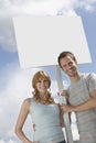 Portrait of happy couple with blank sign over cloudy sky Royalty Free Stock Photo