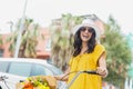Woman posing on sunny street by bicycle basket of flowers wearing yellow sundress, copy space Royalty Free Stock Photo