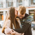 Portrait of happy couple embracing in downtown, red-haired man with glasses kisses and woman with long hair. Girl whispers in ear Royalty Free Stock Photo