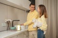 Portrait of happy couple in the kitchen, man washing the dishes, woman holding little white dog, dishwashing liquid Royalty Free Stock Photo