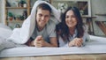 Portrait of happy couple lying in bed under blanket looking at camera laughing and smiling. Loving married people and Royalty Free Stock Photo