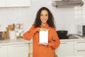 Portrait of a happy curly haired Latin American woman holding a laptop on a white background in the kitchen to add a message. Royalty Free Stock Photo