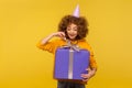 Portrait of happy curly-haired woman unpacking huge gift box with expression full of great expectation Royalty Free Stock Photo