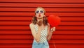 Portrait of happy cute girl with big red heart shaped balloon and girly hairstyle blows her lips sends air kiss wearing sunglasses Royalty Free Stock Photo