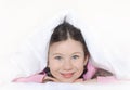 Portrait of a happy cute girl lying on white bed linen under a blanket Royalty Free Stock Photo