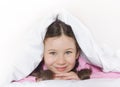 Portrait of a happy cute girl lying on white bed linen under a blanket Royalty Free Stock Photo