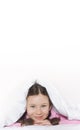 Portrait of a happy cute girl lying on white bed linen under a blanket. Vertical photography. Copy space for text Royalty Free Stock Photo